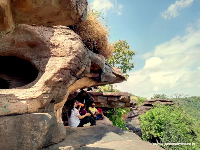 A cave and rock formation with a group climbing the approach.