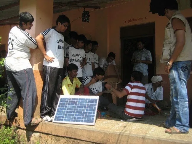Students gathered around a solar panel on a community installation.